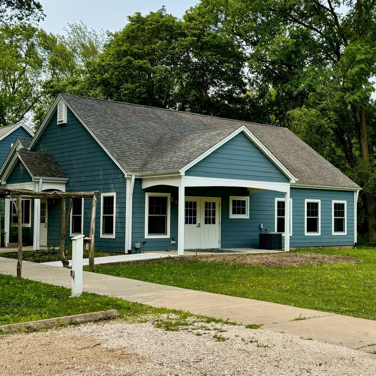Blue house with white trim surrounded by trees and a sidewalk.